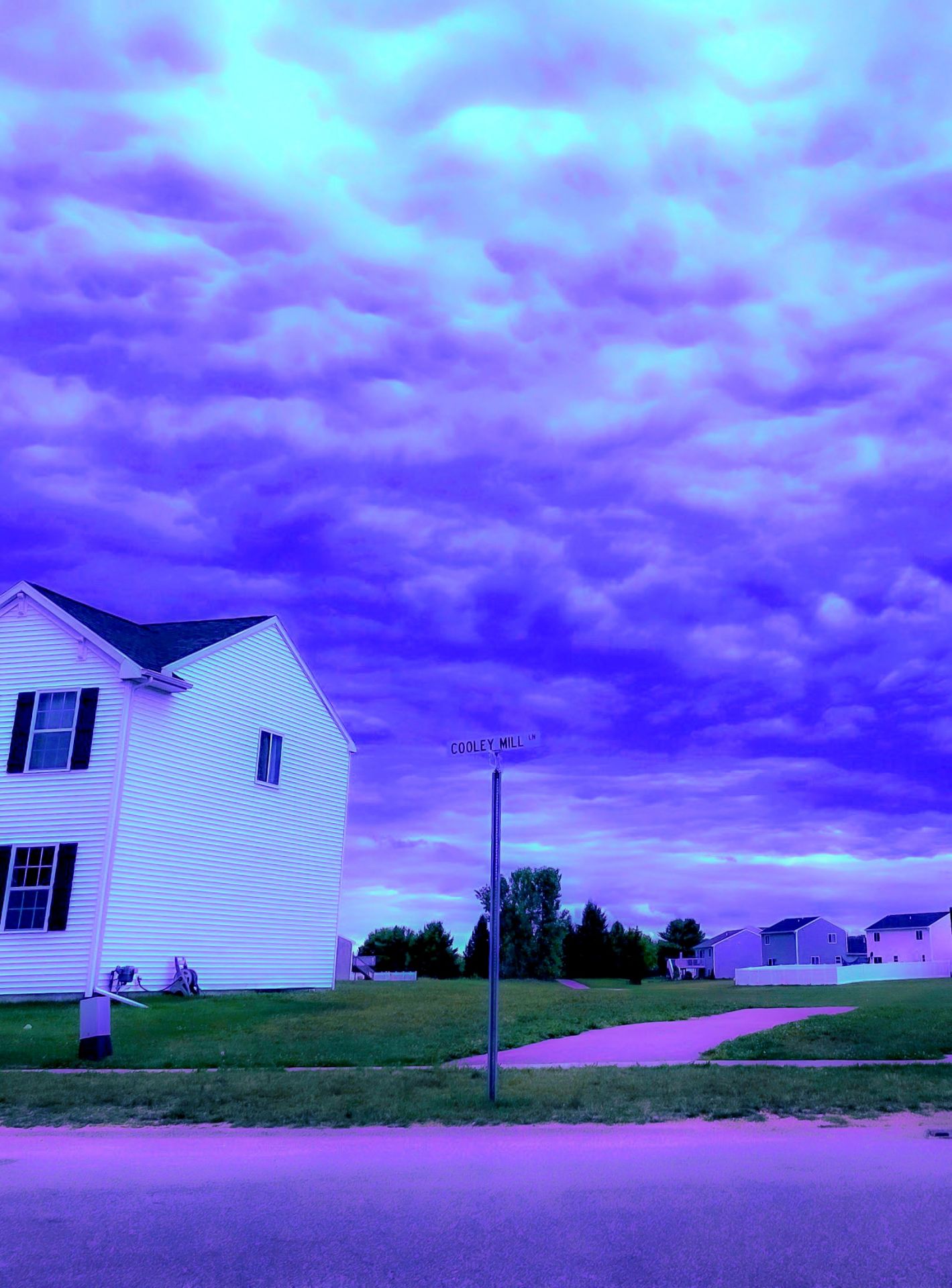 A white house stands beside a Cooley Mill Lane sign under a surreal, vibrant purple sky, creating a dream-like, liminal suburban landscape.