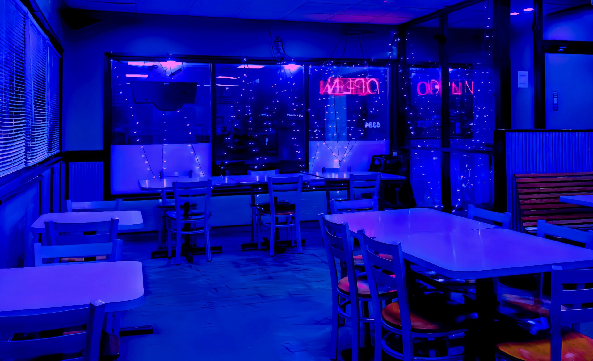 An empty restaurant interior bathed in ethereal blue light, featuring tables, chairs, and a glowing neon "OPEN" sign reflected in dark windows.