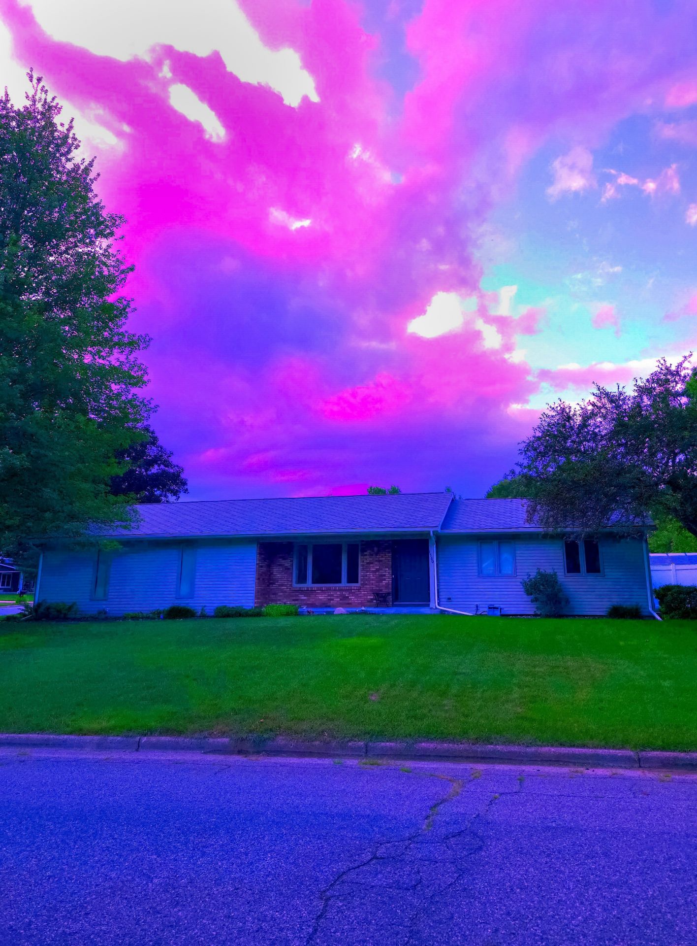 A suburban ranch house sits under a surreal, vibrant magenta and blue sky, creating a dream-like, liminal atmosphere in this twilight residential scene.