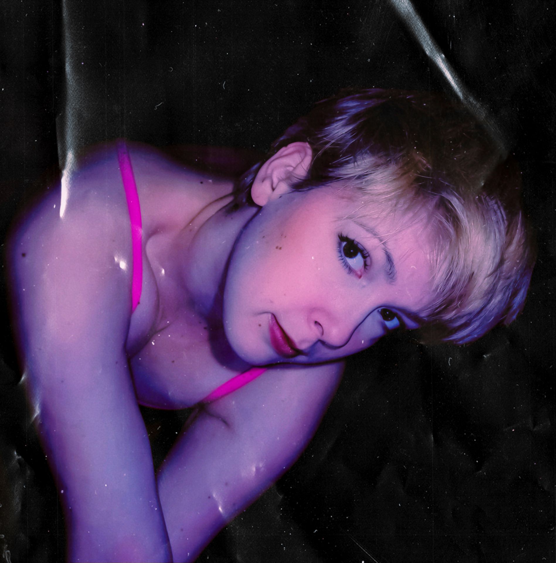 A short-haired woman in a pink top poses against a dark, textured background, bathed in ethereal purple light with a dream-like, vintage aesthetic.